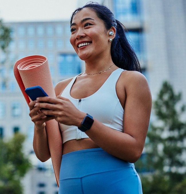 Smiling woman walking on park with workout mat