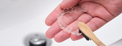 Patient using toothbrush to clean aligners in sink