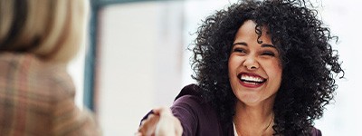 Woman with curly hair in red jacket shaking hand of blond woman