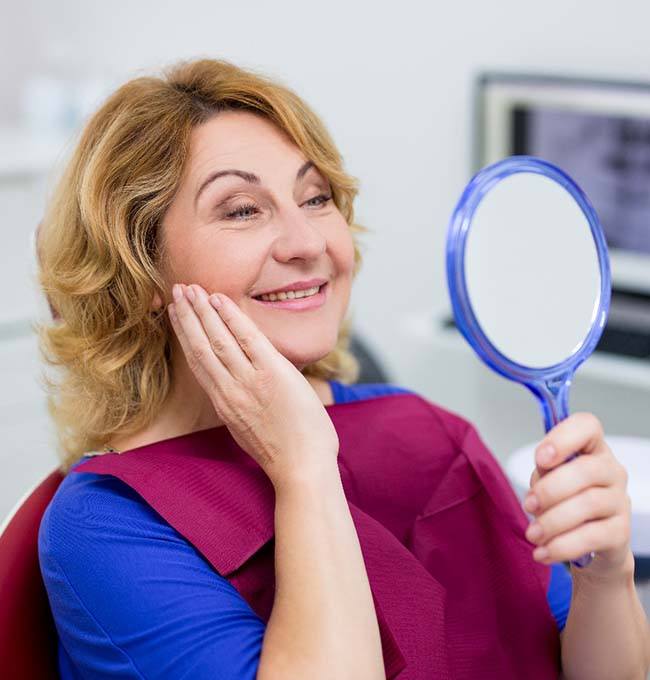 woman with dental implant looking at her smile in a mirror