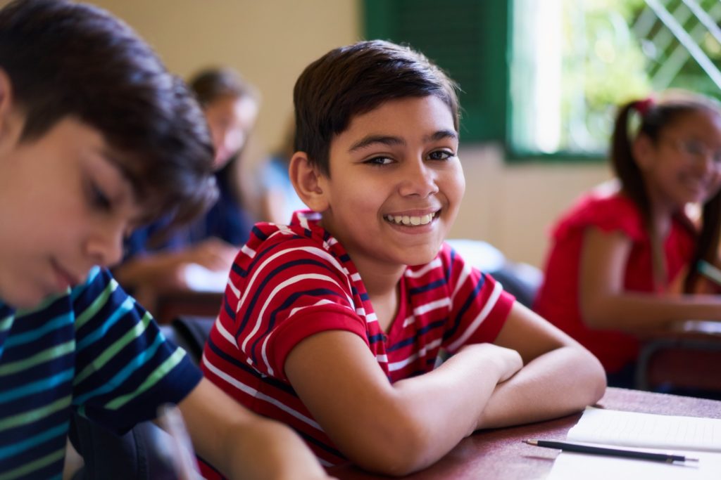 Child smiling while sitting at desk in school