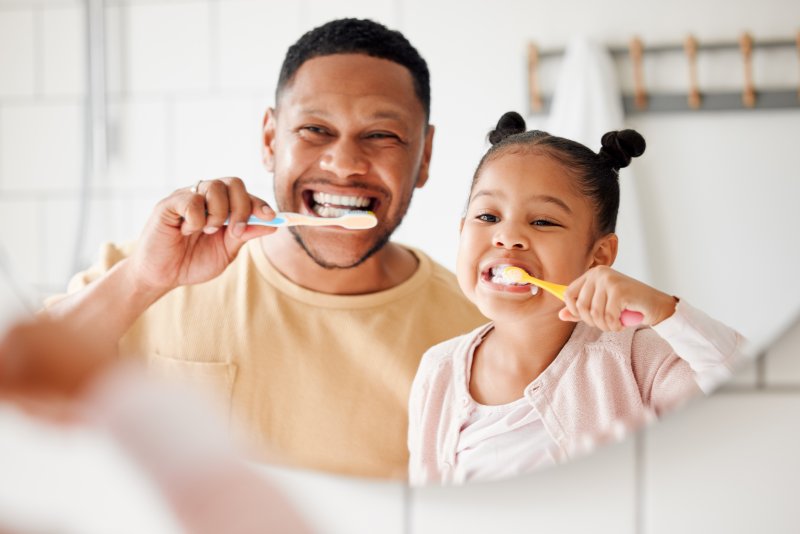 A man and his daughter brushing their teeth together for good dental health
