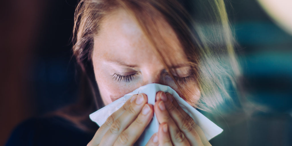 person suffering from seasonal allergies blowing nose