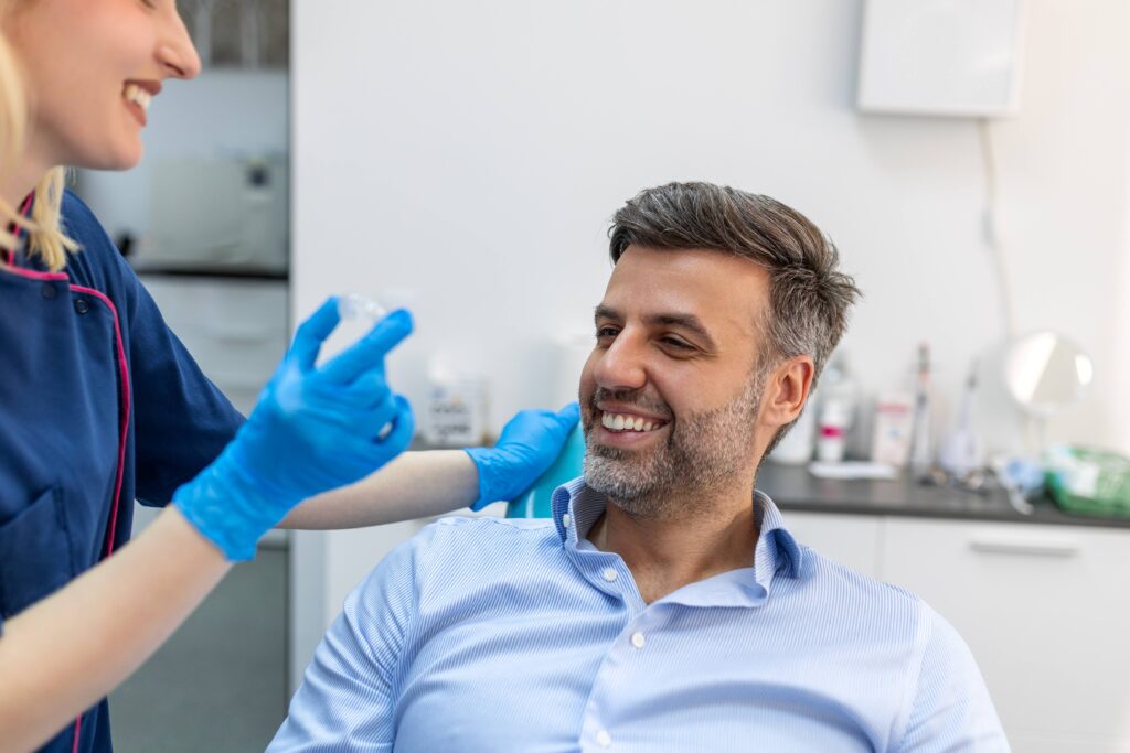 Patient smiling with dental assistant holding clear aligner