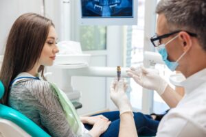 Dentist consulting with patient holding a dental implant.